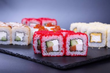 Deniz ürünleri, balık ve kırmızı havyarlı parlak pirinç ruloları koyu bir arka planda yatar.