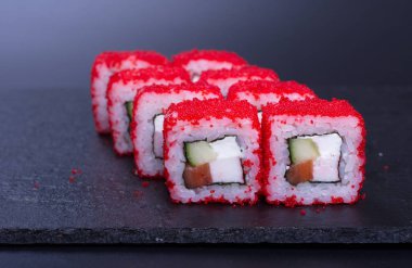 Balık ve kırmızı somon havyarlı pirinç ruloları koyu bir arka planda yatar.