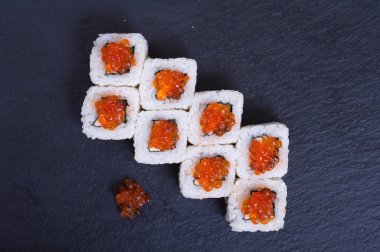 Balık ve kırmızı somon havyarlı pirinç ruloları koyu bir arka planda yatar.