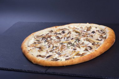 İtalyan pizzası, mantarlı ve beyaz soslu siyah bir taşın üzerinde.