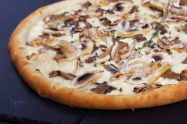 İtalyan pizzası, mantarlı ve beyaz soslu siyah bir taşın üzerinde.