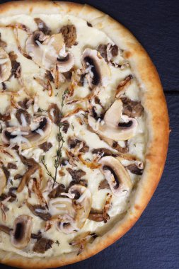 İtalyan pizzası, mantarlı ve beyaz soslu siyah bir taşın üzerinde.