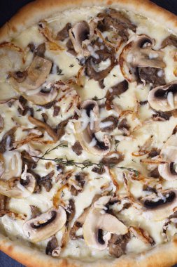 İtalyan pizzası, mantarlı ve beyaz soslu siyah bir taşın üzerinde.