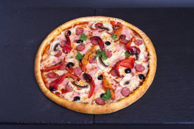 Biber ve jambonlu baharatlı İtalyan pizzası siyah bir taşın üzerinde duruyor.