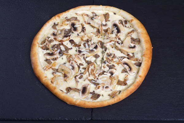 Italian pizza with mushrooms and white sauce lies on a black stone