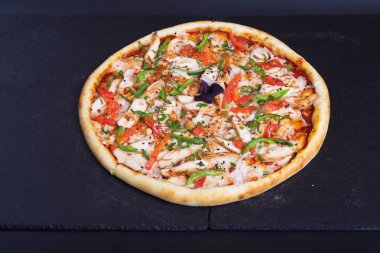 Kırmızı, yeşil biberli ve jambonlu pizza siyah bir taşın üzerinde duruyor.