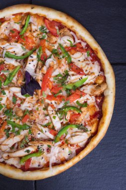 Kırmızı, yeşil biberli ve jambonlu pizza siyah bir taşın üzerinde duruyor.