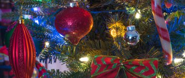 Tatil sezonu, yılbaşı ağacı süsleri parlak ve canlı, altında parlayan küçük faux kapalı ağaç üzerindeki renkli ışıklar.