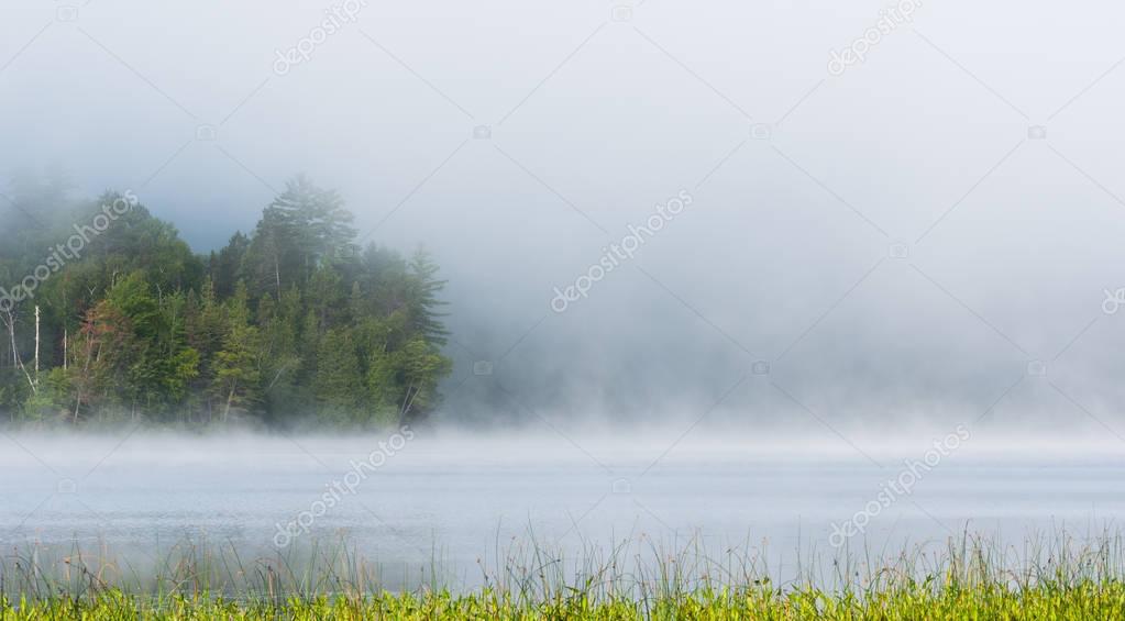 Summer morning foggy mist rises from lake into cool air.