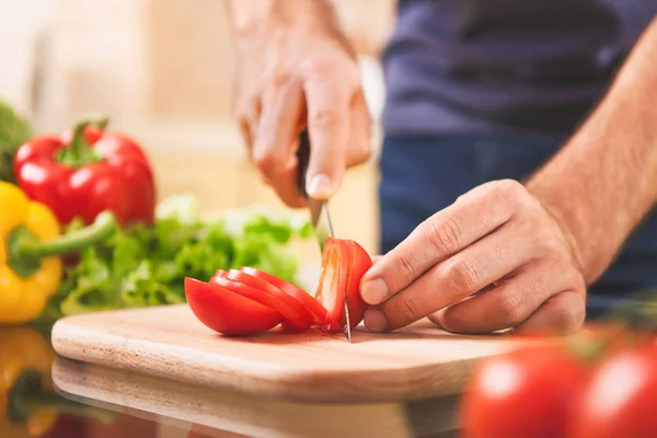 Close up of male hand cutting tomato on cutting board — Stock Photo, Image