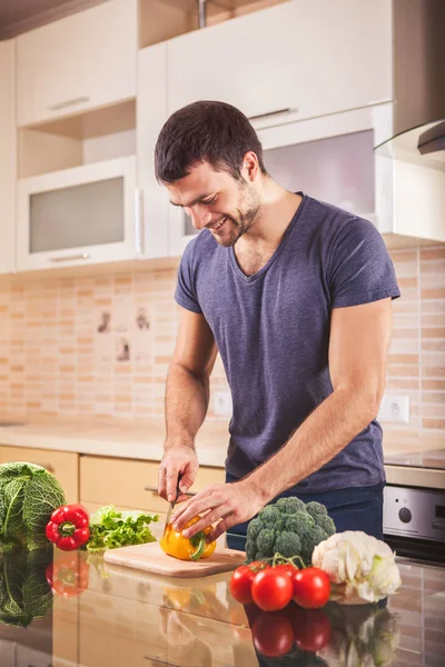 Jovem homem cortando legumes na cozinha — Fotografia de Stock