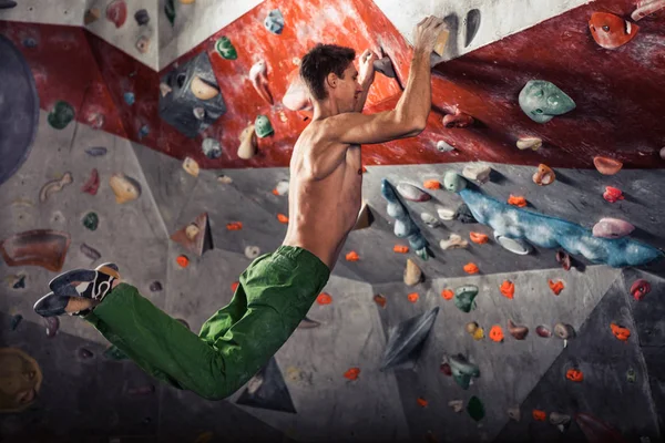 Hombre practicando escalada en roca en una pared de roca en el interior — Foto de Stock