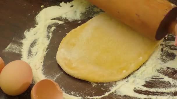 Un cuisinier roule la pâte avec un rouleau à pâtisserie sur une table — Video