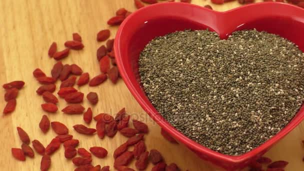 Chia seeds in heart shaped ceramic bowl and dried goji berries — Stock Video