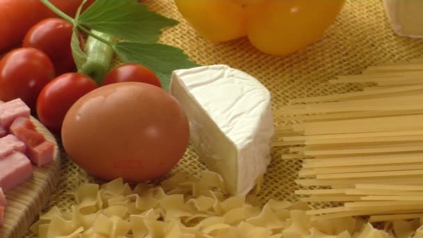 Паста, ветчина, сыр, яйца и овощи с деревенской мешковиной на желтом фоне — стоковое видео