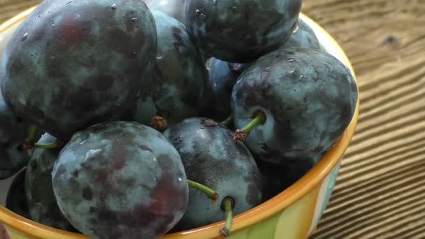 Ciruelas orgánicas frescas en tazón de cerámica sobre mesa de madera rústica — Vídeos de Stock