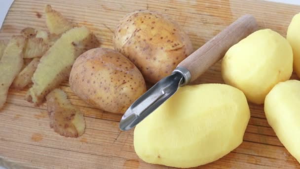 Pelador de patatas y peladuras de tubérculo, acostado sobre una mesa de madera — Vídeo de stock