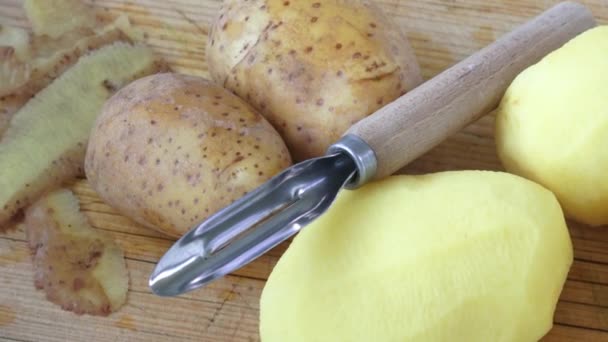 Potatoes with peeler and peeled skin on wooden background — Stock Video