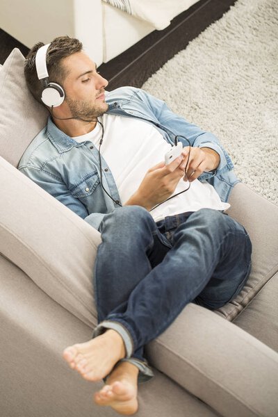 Веселый человек расслабляется на диване, слушает музыку
