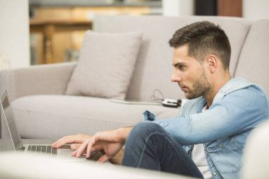 Genç adam salon dizüstü bilgisayar kullanan