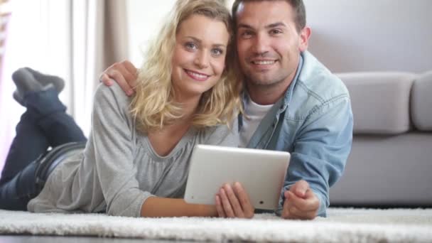 Feliz jovem casal colocado no tapete de sua sala de estar e usando um tablet — Vídeo de Stock