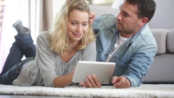 Happy young couple layed on the carpet of their living room and using a tablet — Stock Video