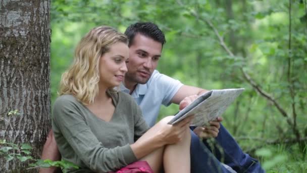 Des randonneurs assis sous un arbre lisant une carte — Video