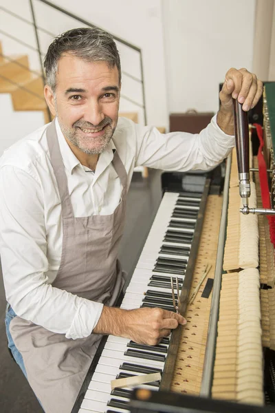 Technician tuning a upright piano using lever and tools