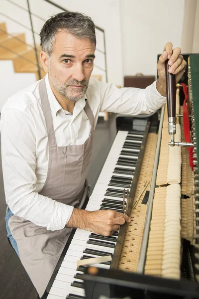 Technician tuning a upright piano using lever and tools