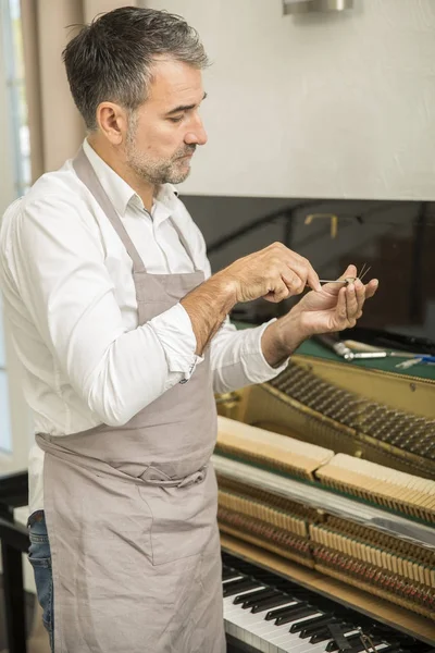 Technician tuning a upright piano using lever and tools