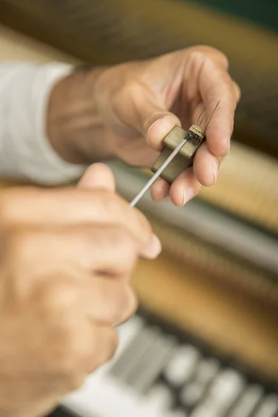 Technician tuning a upright piano using lever and tools