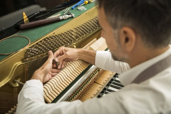 Technician tuning a upright piano using lever and tools