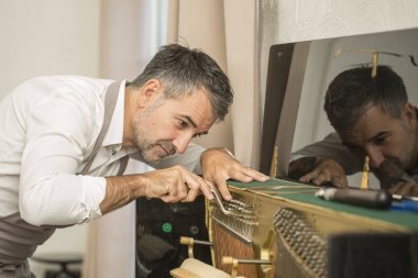 Teknisyen bir dik piyano kolu ve araçlarını kullanarak ayarlama