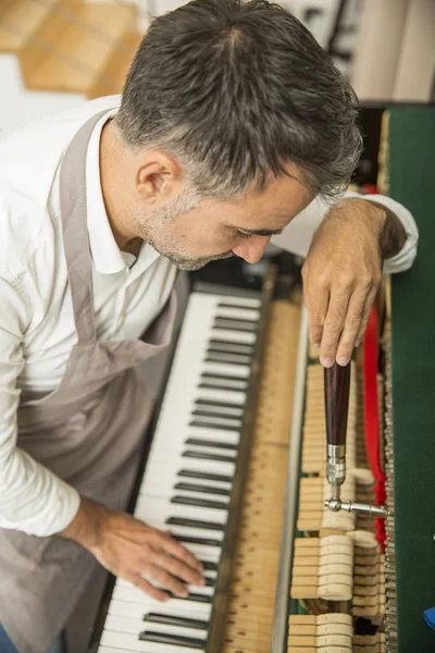 Technician tuning a upright piano using lever and tools