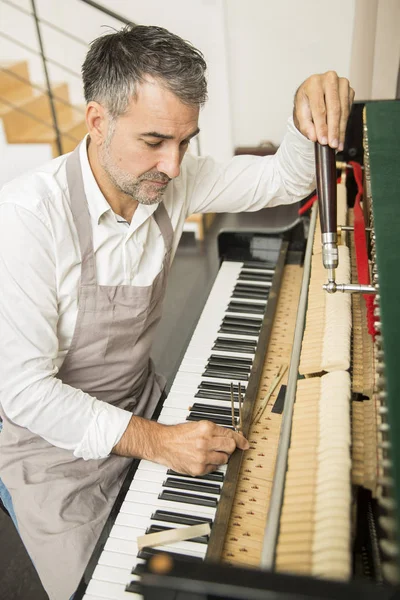 Technician tuning a upright piano using lever and tools