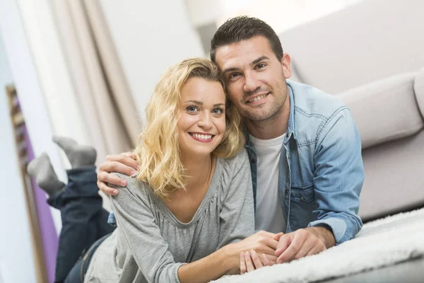 Feliz joven pareja acostada en la alfombra de su sala de estar — Foto de Stock