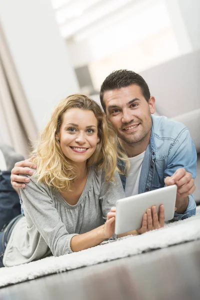 Glada unga par som på mattan i deras vardagsrum och — Stockfoto