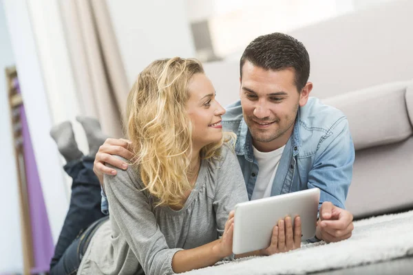 Feliz joven pareja acostado en la alfombra de su sala de estar y — Foto de Stock