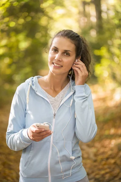 Mujer usando smartphone después de correr en el bosque en otoño Imágenes de stock libres de derechos