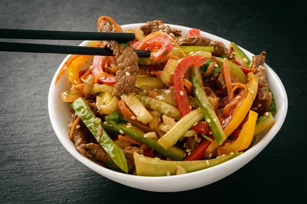 Asian (korean) salad with beef, vegetables and sesame seeds on black board. — Stock Photo, Image
