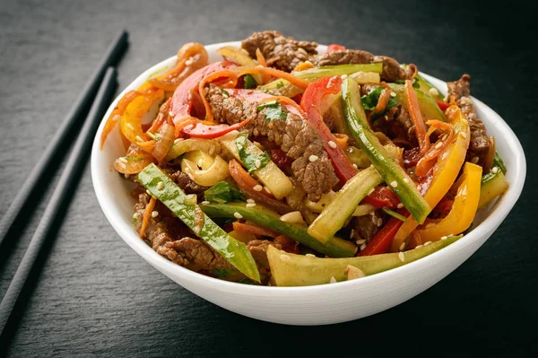 Asian (korean) salad with beef, vegetables and sesame seeds on black board. — Stock Photo, Image