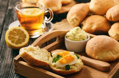 Evde kahvaltı - ev yapımı ekmek rulo, fincan çay, haşlanmış yumurta ve sarımsak ot tereyağı.