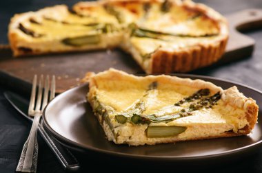 Kuşkonmaz ve siyah arka plan üzerine peynir ile ev yapımı tart.