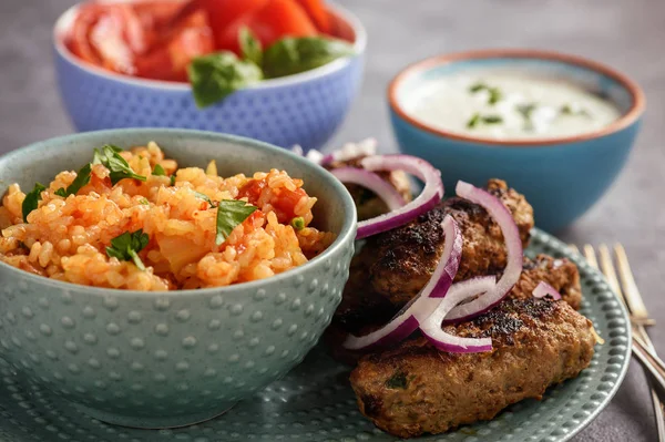 Cevapcici, balkanian grilled meat sausages with savory rice and yogurt dip.