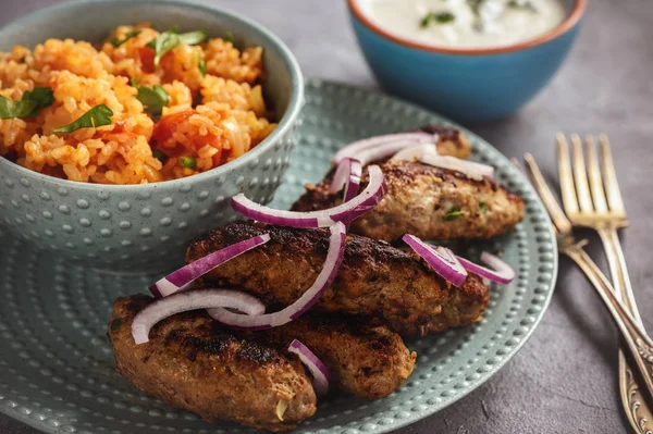 Cevapcici, balkanian grilled meat sausages with savory rice and yogurt dip.