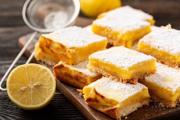 Homemade lemon bars with shortbread crust, on wooden background.