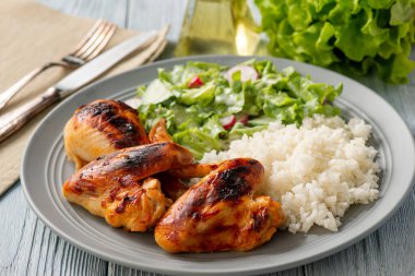 Izgara tavuk kanadı ve but, haşlanmış pirinç ve salata ile servis edilir..