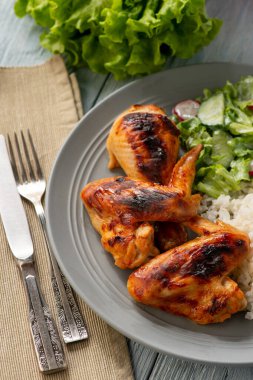 Izgara tavuk kanadı ve but, haşlanmış pirinç ve salata ile servis edilir..