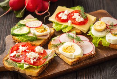 Toasts with eggs, cheese, ham, radish, cucumbers and tomatoes , breakfast idea.