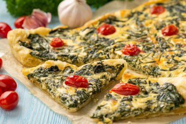 Homemade spinach puff pastry tart with cheese and tomatoes.